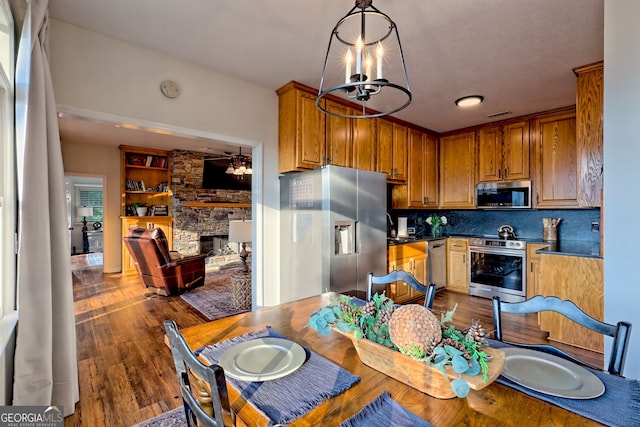 63 Maple Ridge Trl, Clayton, GA 30525 - kitchen featuring appliances with stainless steel finishes, a chandelier, a stone fireplace, dark wood finished floors, and decorative backsplash
