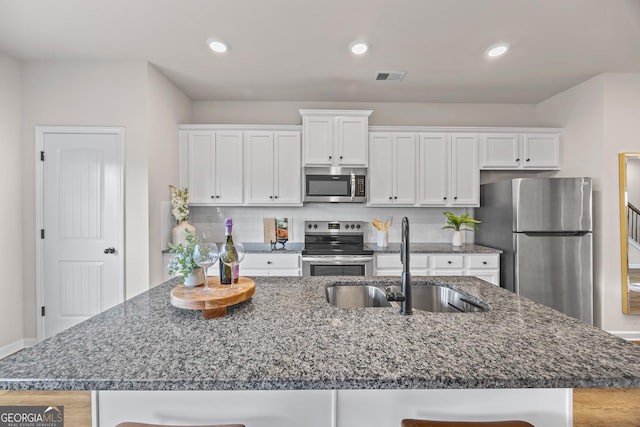 1004 Bayrose Cir, East Point, GA 30344 - kitchen with stainless steel appliances, white cabinets, a center island with sink, dark stone counters, and recessed lighting