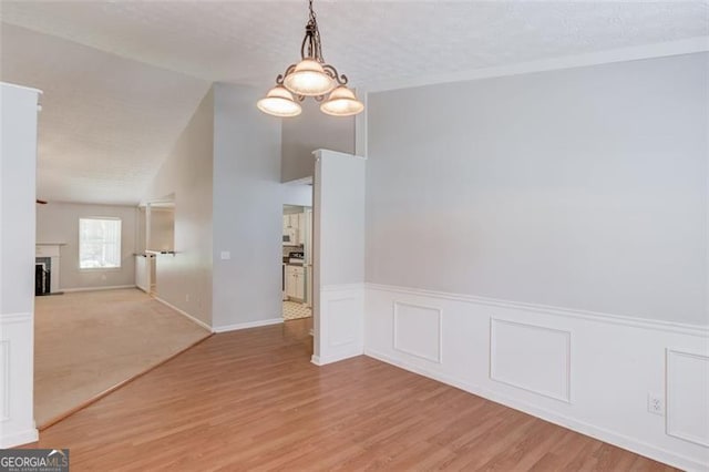 738 Baskins, Winder, GA 30680 - unfurnished room featuring light wood-style flooring, a fireplace, a chandelier, wainscoting, and a textured ceiling