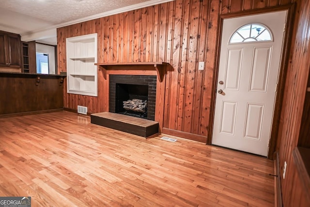 500 Holmes St, Barnesville, GA 30204 - unfurnished living room with crown molding, wooden walls, healthy amount of natural light, light wood-type flooring, and a brick fireplace