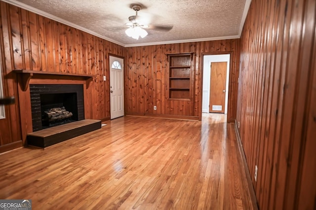 500 Holmes St, Barnesville, GA 30204 - unfurnished living room featuring ornamental molding, wooden walls, a textured ceiling, a fireplace, and wood finished floors