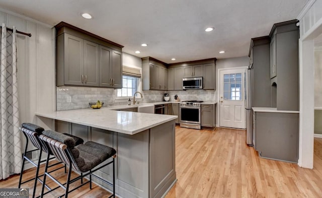 595 Glenforest Rd, Sandy Springs, GA 30328 - kitchen with appliances with stainless steel finishes, a peninsula, light wood-style flooring, decorative backsplash, and a kitchen bar