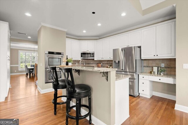 411 Hickory Fairway Ct, Woodstock, GA 30188 - kitchen featuring appliances with stainless steel finishes, white cabinets, light wood-type flooring, backsplash, and ornamental molding
