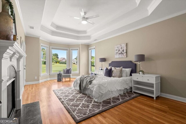 411 Hickory Fairway Ct, Woodstock, GA 30188 - bedroom with a tray ceiling, wood finished floors, crown molding, a fireplace with flush hearth, and a ceiling fan