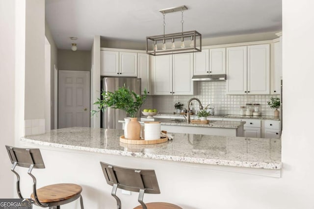 2000 Settindown Dr, Roswell, GA 30075 - kitchen with freestanding refrigerator, under cabinet range hood, decorative backsplash, and light stone counters
