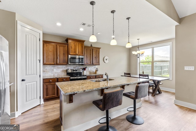 206 Barnyard Way, Perry, GA 31069 - kitchen with appliances with stainless steel finishes, light wood-style floors, brown cabinets, decorative backsplash, and a breakfast bar area