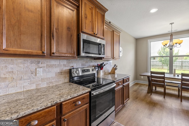 206 Barnyard Way, Perry, GA 31069 - kitchen featuring appliances with stainless steel finishes, brown cabinets, a chandelier, wood finished floors, and backsplash
