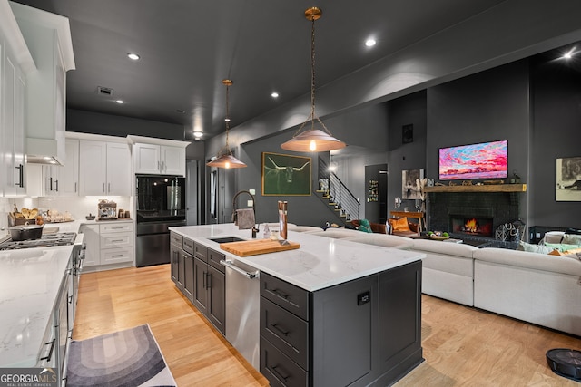 40 Fernbank Way, Newnan, GA 30265 - kitchen with stainless steel appliances, white cabinetry, a warm lit fireplace, a center island with sink, and light wood-type flooring