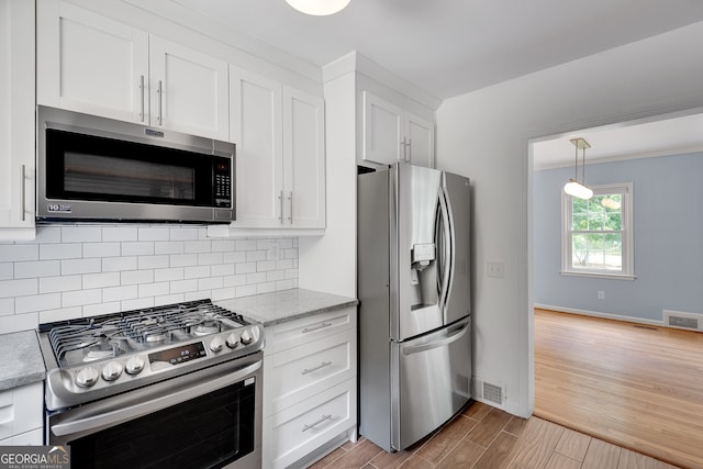 1131 Forrest Blvd, Decatur, GA 30030 - kitchen featuring stainless steel appliances, wood finished floors, white cabinets, decorative backsplash, and hanging light fixtures