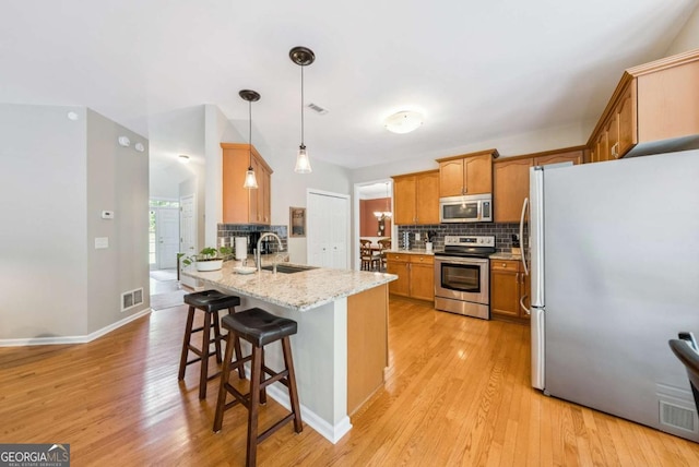 9320 Old Preserve Trl, Ball Ground, GA 30107 - kitchen featuring stainless steel appliances, a peninsula, tasteful backsplash, a breakfast bar area, and light wood-style flooring