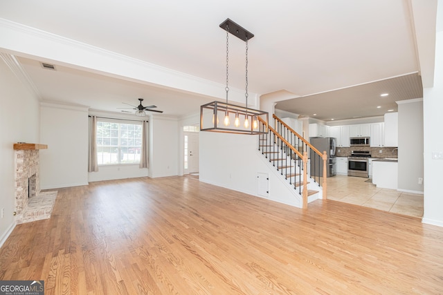 2427 Camata Pl, Marietta, GA 30066 - unfurnished living room with stairs, a ceiling fan, ornamental molding, a fireplace with raised hearth, and light wood-style floors
