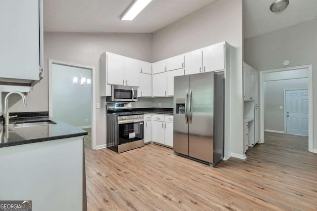 5215 Mainstreet Park Dr, Stone Mountain, GA 30088 - kitchen featuring appliances with stainless steel finishes, light wood finished floors, white cabinets, high vaulted ceiling, and dark stone countertops