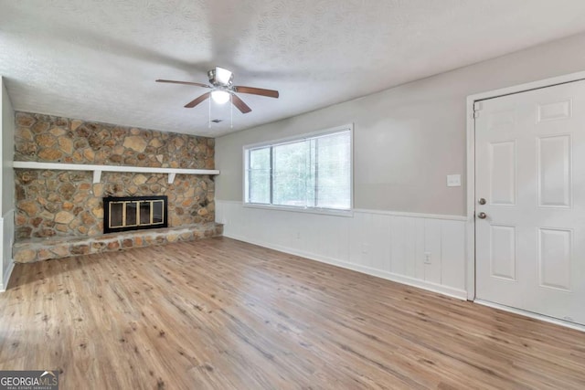 5215 Mainstreet Park Dr, Stone Mountain, GA 30088 - unfurnished living room featuring wood finished floors, ceiling fan, wainscoting, a textured ceiling, and a stone fireplace