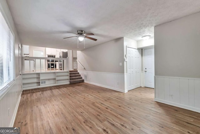 5215 Mainstreet Park Dr, Stone Mountain, GA 30088 - unfurnished living room featuring wood finished floors, a ceiling fan, a wainscoted wall, and stairs