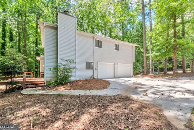 5215 Mainstreet Park Dr, Stone Mountain, GA 30088 - view of side of home with concrete driveway, a chimney, a garage, a wooden deck, and view of scattered trees