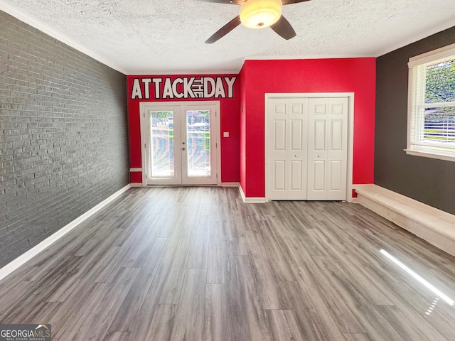 314 Pine St, Barnesville, GA 30204 - unfurnished bedroom with a textured ceiling, french doors, brick wall, an accent wall, and wood finished floors