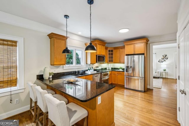 261 Elmira Pl NE, Atlanta, GA 30307 - kitchen featuring stainless steel appliances, a peninsula, brown cabinetry, dark stone counters, and pendant lighting