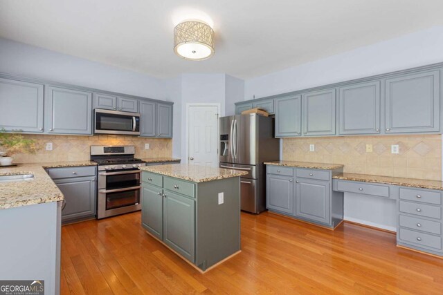 5003 Pacific Dunes Dr, Suwanee, GA 30024 - kitchen with appliances with stainless steel finishes, tasteful backsplash, light wood-type flooring, a kitchen island, and light stone counters