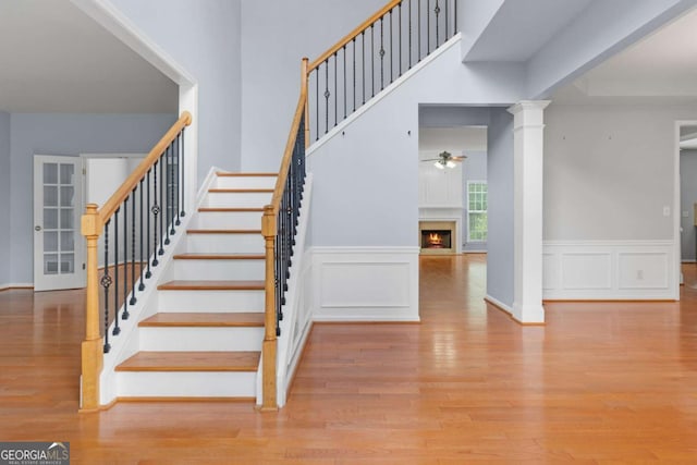 5003 Pacific Dunes Dr, Suwanee, GA 30024 - stairs featuring ceiling fan, wood finished floors, a warm lit fireplace, a decorative wall, and wainscoting
