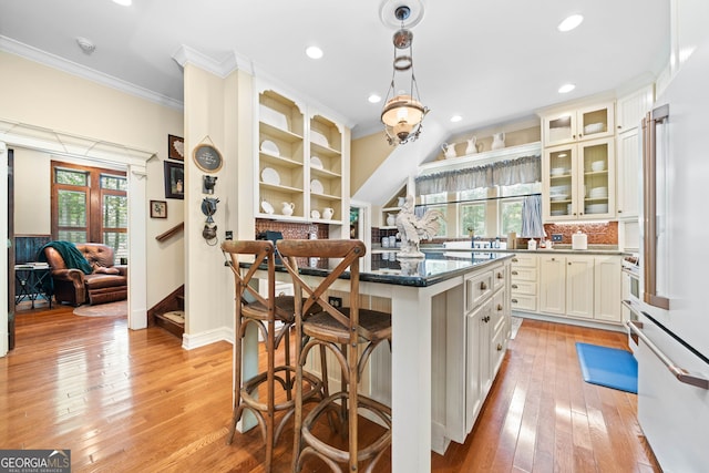 3349 Whitepath Rd, Ellijay, GA 30540 - kitchen with crown molding, a center island, a kitchen breakfast bar, light wood-type flooring, and glass insert cabinets