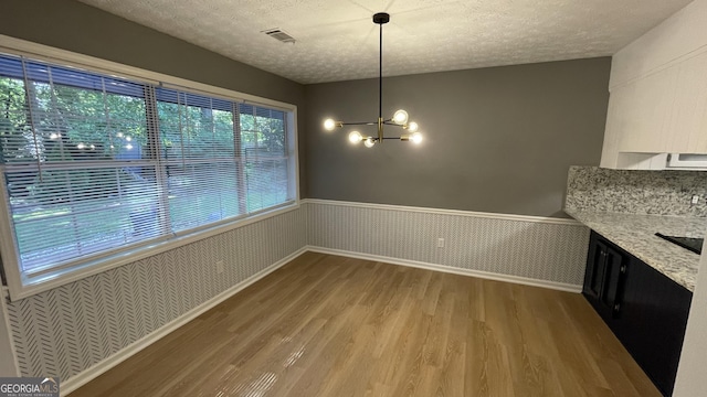 4710 Cedar Brook Dr SE, Conyers, GA 30094 - unfurnished dining area with wood finished floors, a wainscoted wall, a chandelier, and a textured ceiling