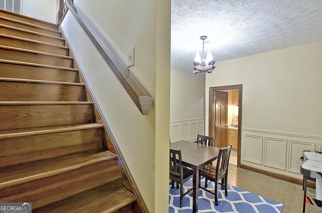 115 Shoal Creek Dr, Sharpsburg, GA 30277 - stairway featuring a chandelier, a textured ceiling, a wainscoted wall, and a decorative wall