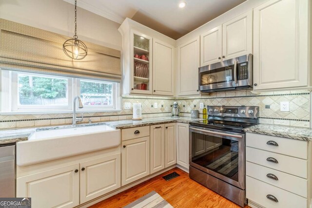1461 Radstone Dr, Lawrenceville, GA 30044 - kitchen with stainless steel appliances, decorative backsplash, light wood-style floors, pendant lighting, and glass insert cabinets