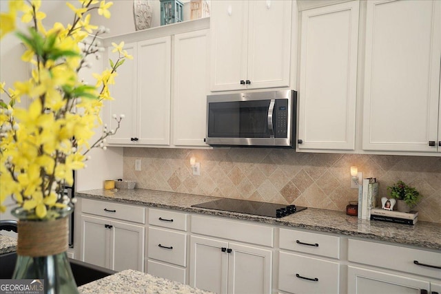 112 Sterling Lake Way, Jefferson, GA 30549 - kitchen featuring stainless steel microwave, black electric cooktop, backsplash, and white cabinetry