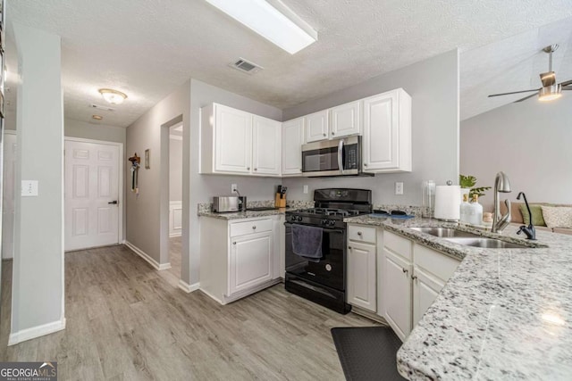 2895 Dominion Walk Ln, Snellville, GA 30078 - kitchen with black gas stove, stainless steel microwave, light wood-type flooring, white cabinetry, and a textured ceiling