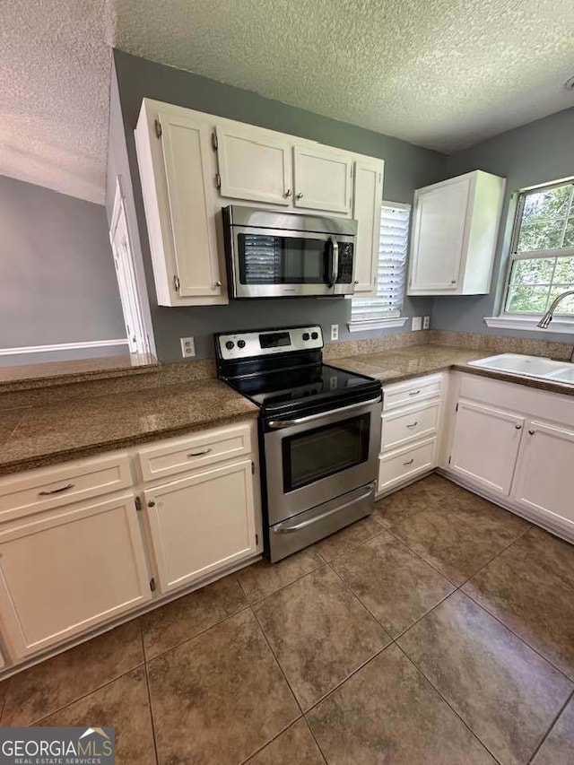 160 Lake Wellington Dr, Kingsland, GA 31548 - kitchen featuring stainless steel appliances, a textured ceiling, white cabinetry, dark tile patterned flooring, and dark countertops