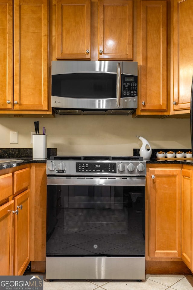 1445 Monroe Dr Unit 14B, Atlanta, GA 30324 - kitchen featuring stainless steel appliances, dark stone countertops, light tile patterned floors, and brown cabinets