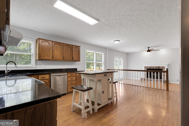 115 Rockhurst Chase, Tyrone, GA 30290 - kitchen featuring stainless steel dishwasher, light wood-style flooring, ceiling fan, dark countertops, and a brick fireplace