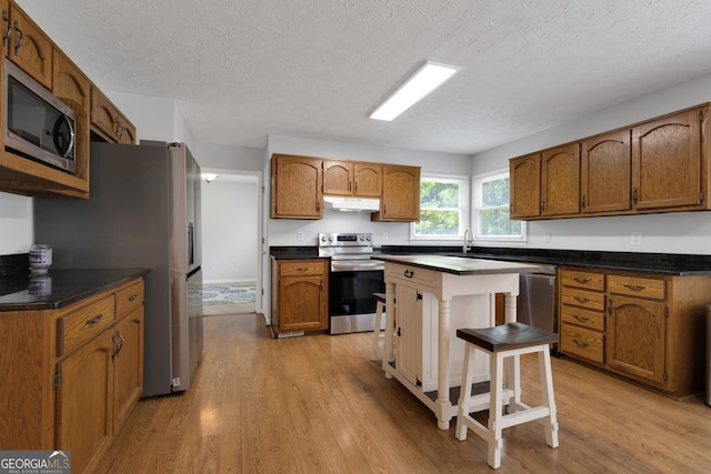 115 Rockhurst Chase, Tyrone, GA 30290 - kitchen with appliances with stainless steel finishes, under cabinet range hood, light wood-type flooring, a textured ceiling, and brown cabinets