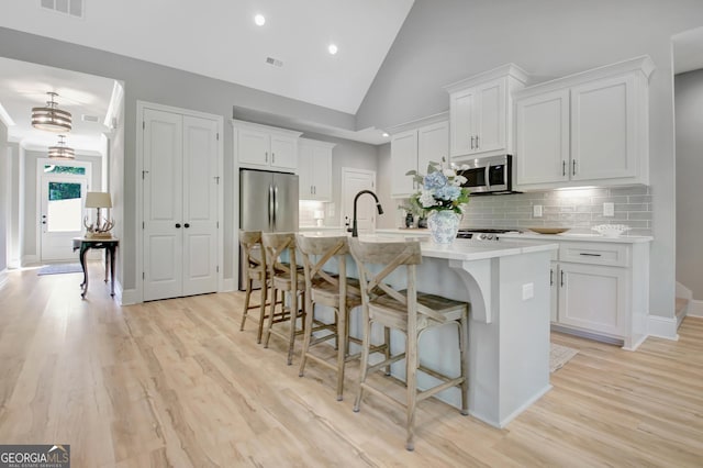 192 Greyfairs Ave, Senoia, GA 30276 - kitchen featuring appliances with stainless steel finishes, a kitchen island with sink, white cabinetry, light countertops, and light wood-type flooring