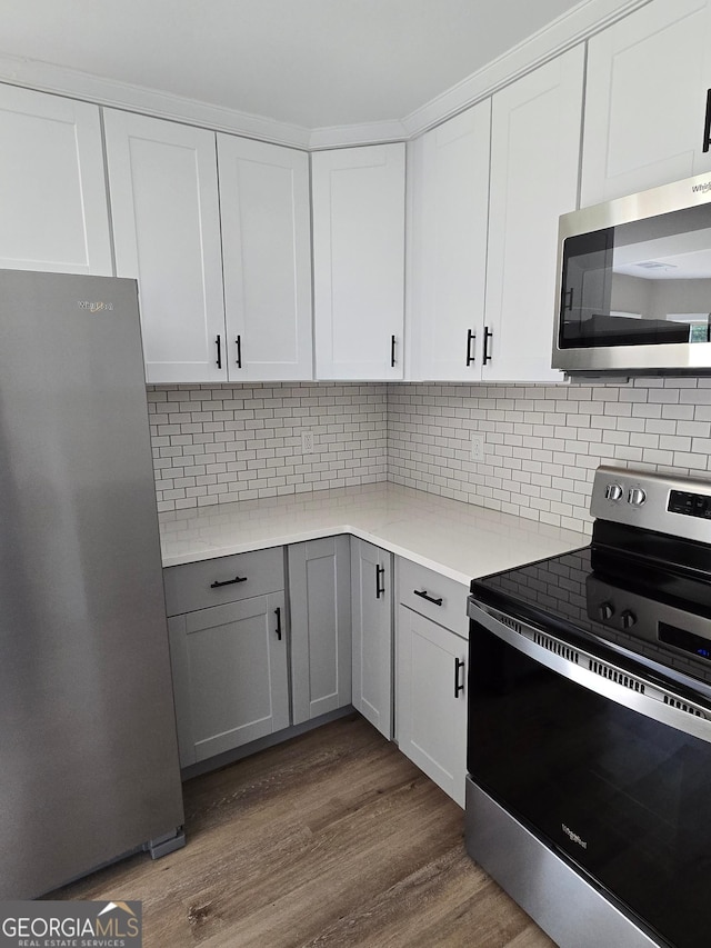 388 Kay Dr, Winder, GA 30680 - kitchen featuring appliances with stainless steel finishes, dark wood-type flooring, light countertops, tasteful backsplash, and white cabinetry