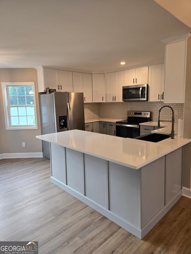 388 Kay Dr, Winder, GA 30680 - kitchen with stainless steel appliances, light wood-type flooring, light countertops, tasteful backsplash, and a peninsula