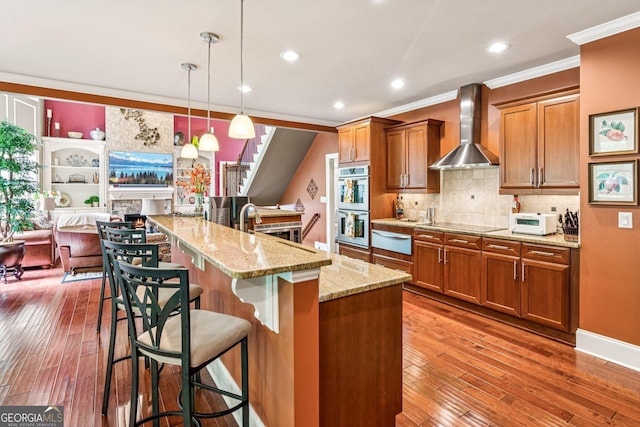 5717 Meadow View Dr, Jefferson, GA 30549 - kitchen with wall chimney exhaust hood, a warming drawer, brown cabinetry, ornamental molding, and hardwood / wood-style flooring