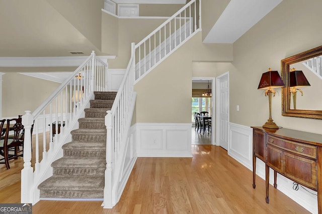 7325 Brookwood Way, Cumming, GA 30041 - staircase with wood finished floors, a wainscoted wall, a decorative wall, and a towering ceiling