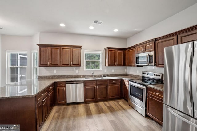 176 Windy Cir, Mcdonough, GA 30253 - kitchen featuring appliances with stainless steel finishes, light wood-style floors, stone counters, decorative backsplash, and a peninsula
