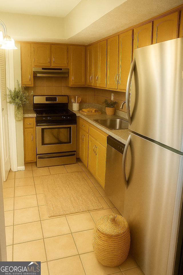 5581 Marbut Rd, Lithonia, GA 30058 - kitchen with appliances with stainless steel finishes, under cabinet range hood, light tile patterned flooring, backsplash, and brown cabinets