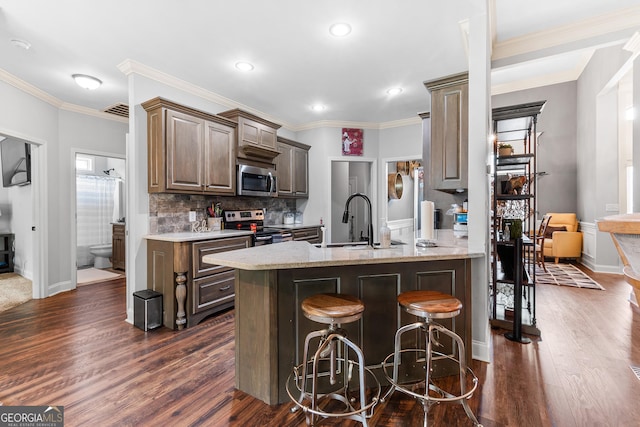 300 Bridgehampton Way, Perry, GA 31069 - kitchen featuring appliances with stainless steel finishes, dark wood finished floors, backsplash, a kitchen bar, and crown molding