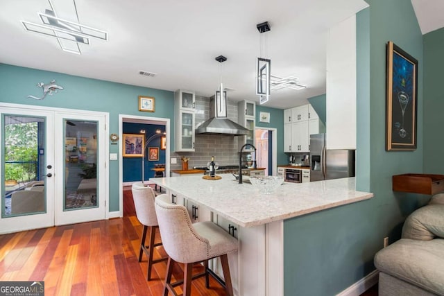 425 Starfire Ct, Suwanee, GA 30024 - kitchen with wall chimney exhaust hood, stainless steel fridge with ice dispenser, a peninsula, white cabinets, and light stone counters