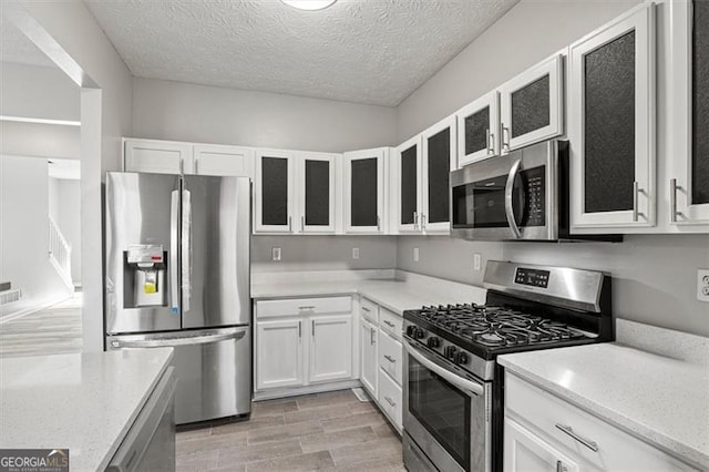 5667 Cascade, Atlanta, GA 30336 - kitchen featuring stainless steel appliances, white cabinets, glass insert cabinets, a textured ceiling, and light wood-style floors