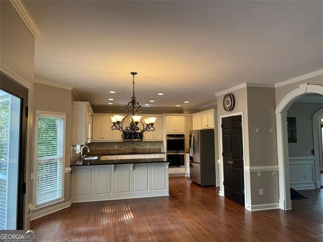 1464 Chatsworth Trce, Lawrenceville, GA 30044 - kitchen featuring appliances with stainless steel finishes, a peninsula, dark countertops, a chandelier, and arched walkways