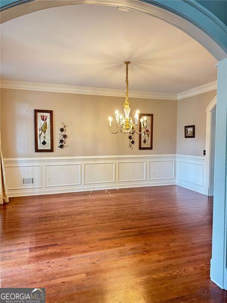 1464 Chatsworth Trce, Lawrenceville, GA 30044 - unfurnished dining area featuring arched walkways, a chandelier, ornamental molding, wood finished floors, and a wainscoted wall
