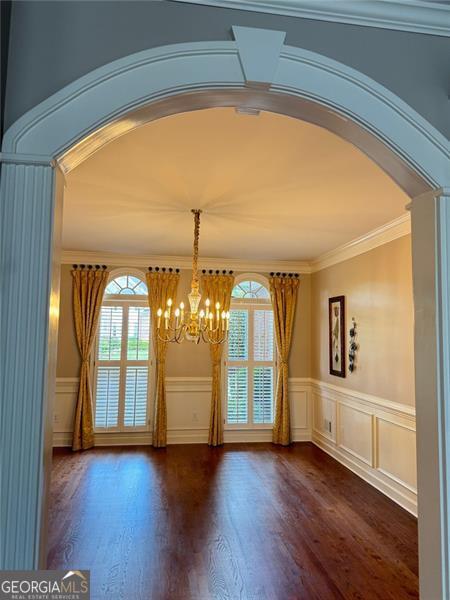 1464 Chatsworth Trce, Lawrenceville, GA 30044 - unfurnished dining area featuring arched walkways, a chandelier, a wainscoted wall, dark wood-style flooring, and ornamental molding