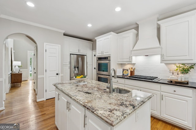 665 Greenview Ter, Milton, GA 30004 - kitchen with appliances with stainless steel finishes, custom range hood, arched walkways, a center island with sink, and light wood-type flooring