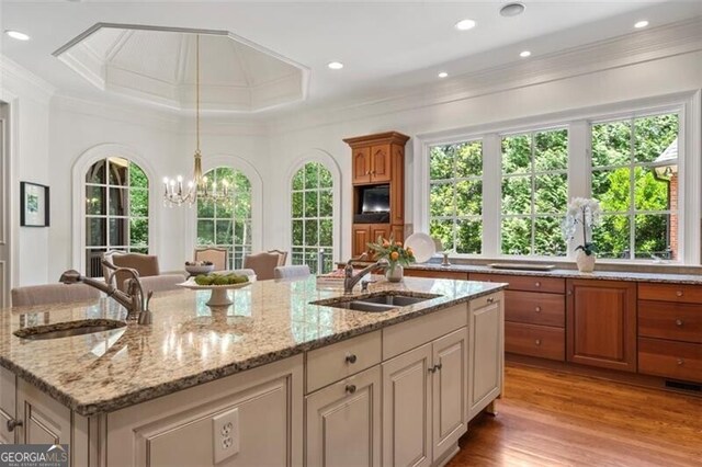 4634 Whitestone Way, Suwanee, GA 30024 - kitchen with crown molding, a chandelier, an island with sink, light stone counters, and light wood-style floors