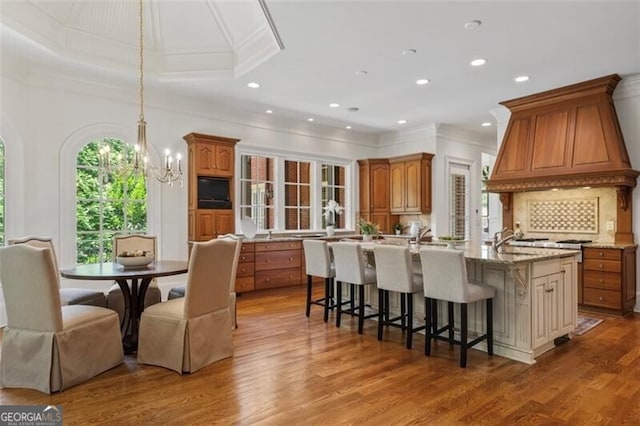 4634 Whitestone Way, Suwanee, GA 30024 - kitchen with crown molding, brown cabinetry, a center island with sink, a chandelier, and recessed lighting