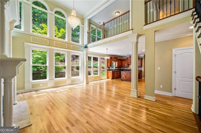 205 Camden Creek Ct, Lawrenceville, GA 30043 - unfurnished living room featuring decorative columns, a towering ceiling, ornamental molding, plenty of natural light, and a chandelier